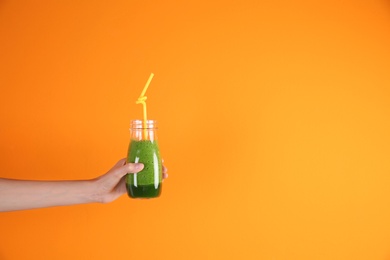 Photo of Young woman holding bottle of healthy smoothie on color background