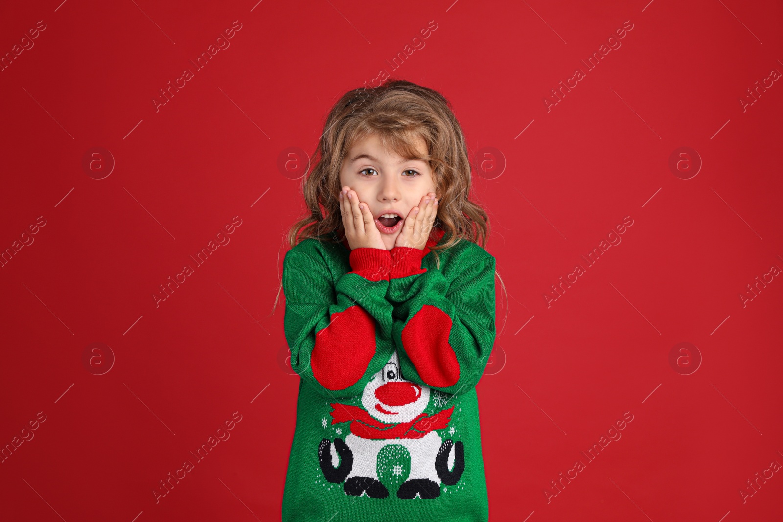 Photo of Surprised little girl in green Christmas sweater against red background