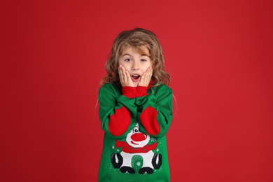 Photo of Surprised little girl in green Christmas sweater against red background