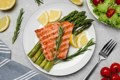 Tasty grilled salmon with asparagus, lemon and rosemary on light grey table, flat lay