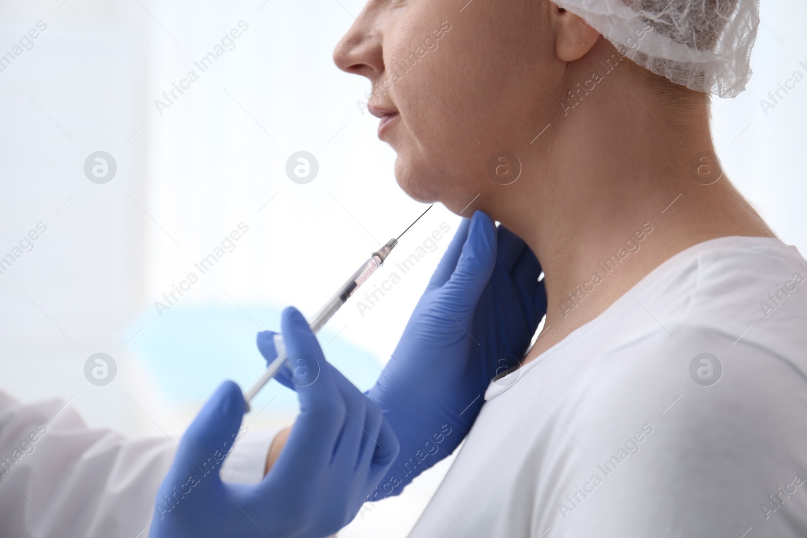 Photo of Mature woman with double chin receiving injection in clinic, closeup