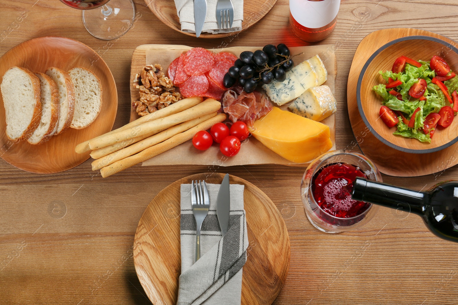 Photo of Pouring red wine into glass on table with delicious food, top view