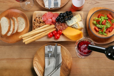 Pouring red wine into glass on table with delicious food, top view