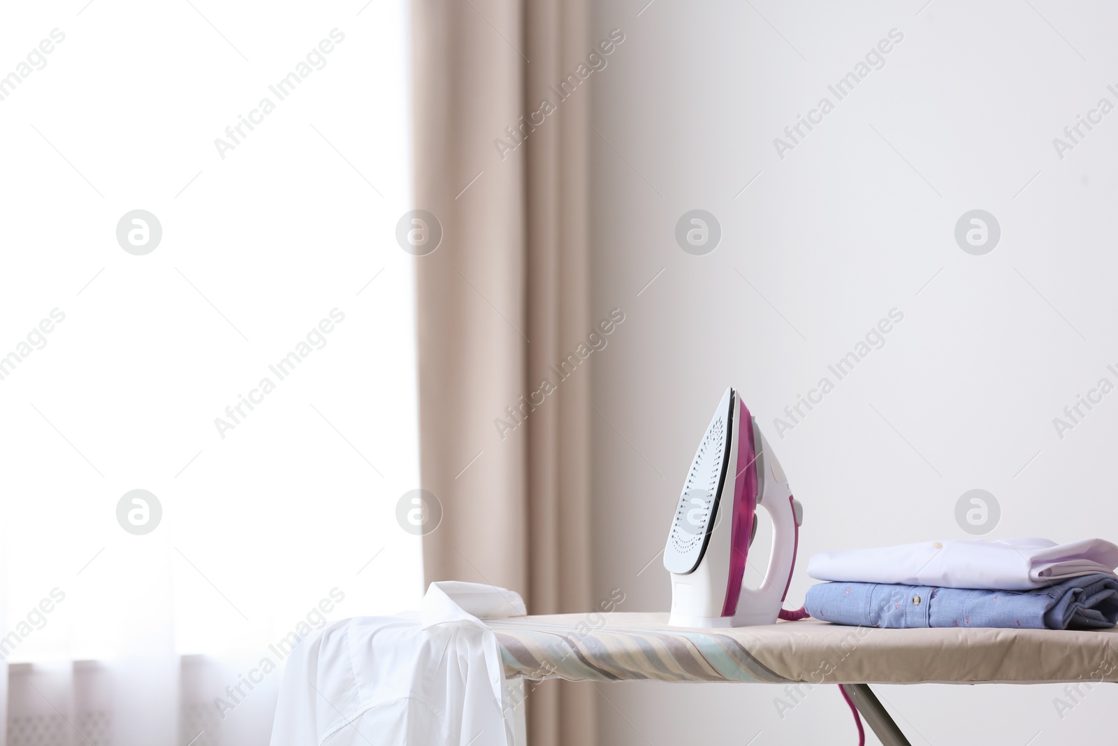 Photo of Modern iron and shirts on board in room. Space for text