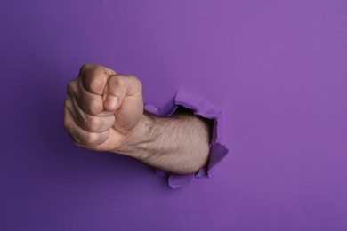 Man breaking through purple paper with fist, closeup