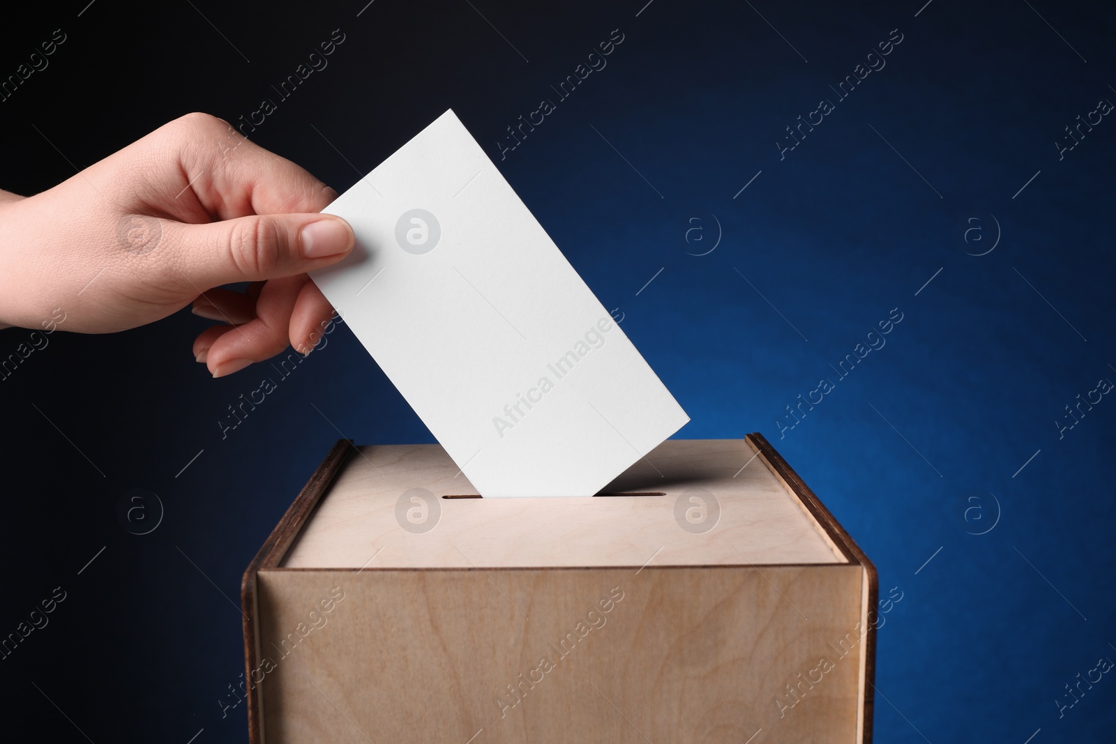 Photo of Woman putting her vote into ballot box on dark blue background, closeup