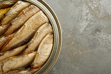 Photo of Sprats in tin can on grey textured table, top view. Space for text