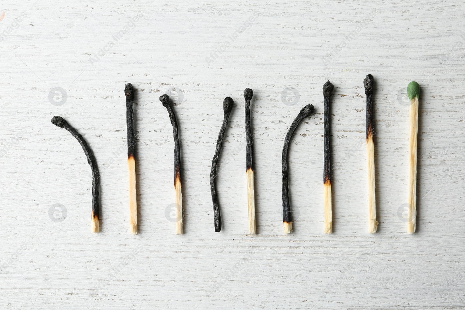 Photo of Row of burnt matches and whole one on wooden background, flat lay. Uniqueness concept