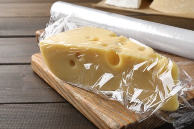 Photo of Block of cheese with plastic food wrap on wooden table, closeup