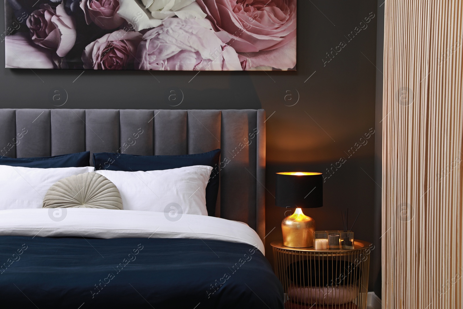 Photo of Comfortable bed with cushions, lamp and different decor on bedside table in room. Stylish interior