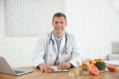 Photo of Nutritionist with clipboard and laptop at desk in office