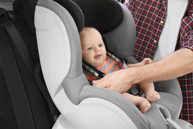 Father fastening baby to child safety seat inside of car