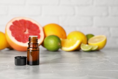 Bottle of essential oil with different citrus fruits on grey marble table. Space for text