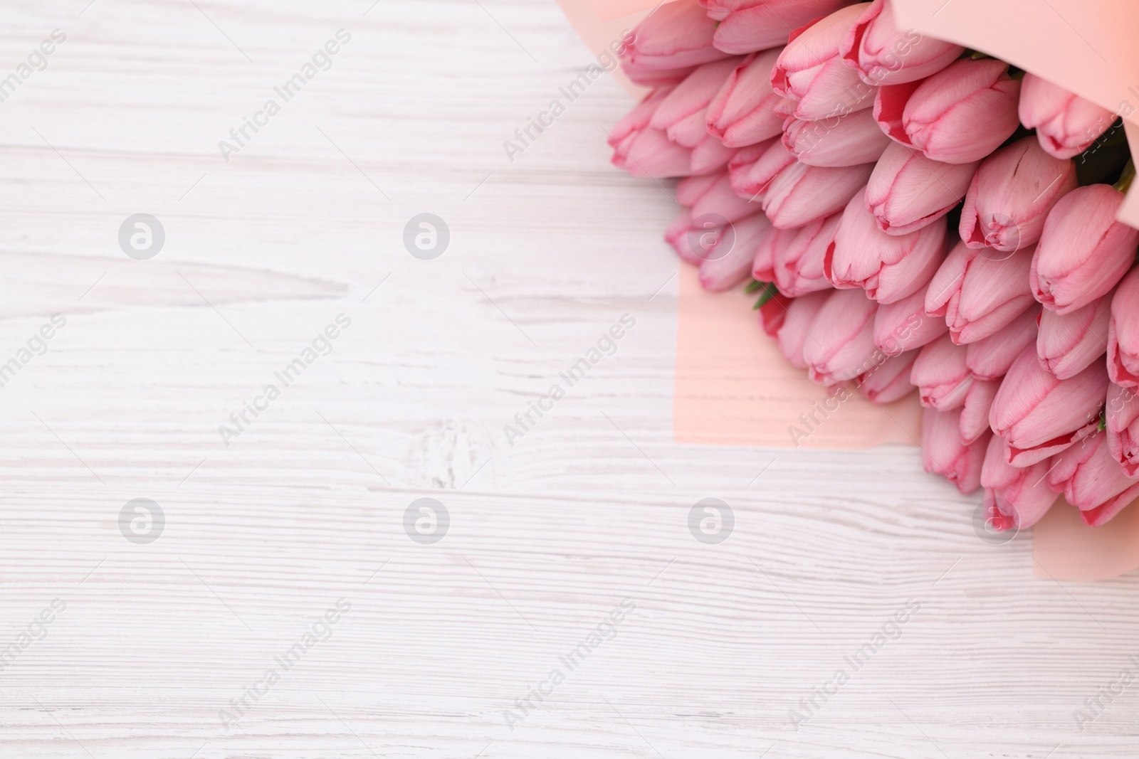 Photo of Bouquet of beautiful pink tulips on white wooden table, above view. Space for text