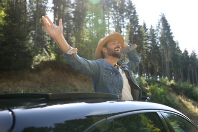 Enjoying trip. Happy man leaning out of car roof on sunny day