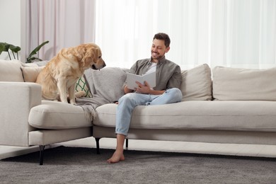 Photo of Man reading book on sofa near his cute Labrador Retriever at home