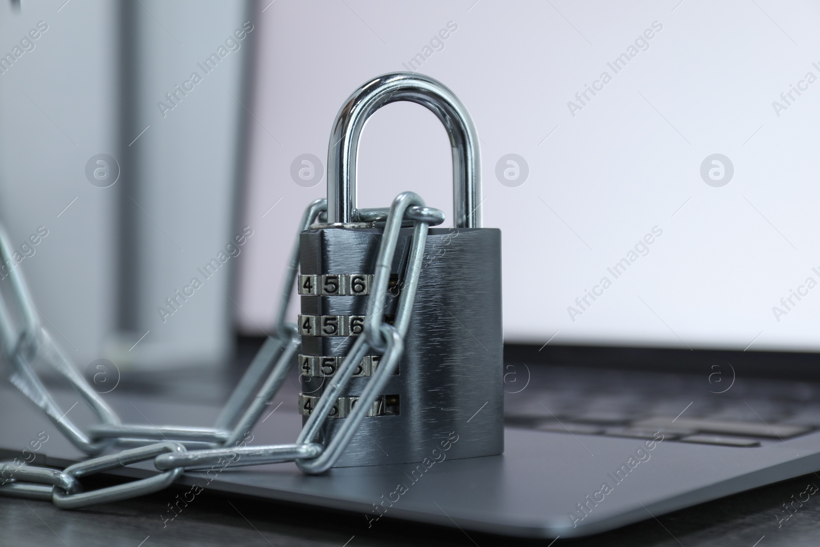 Photo of Cyber security. Metal combination padlock with chain and laptop on table, closeup