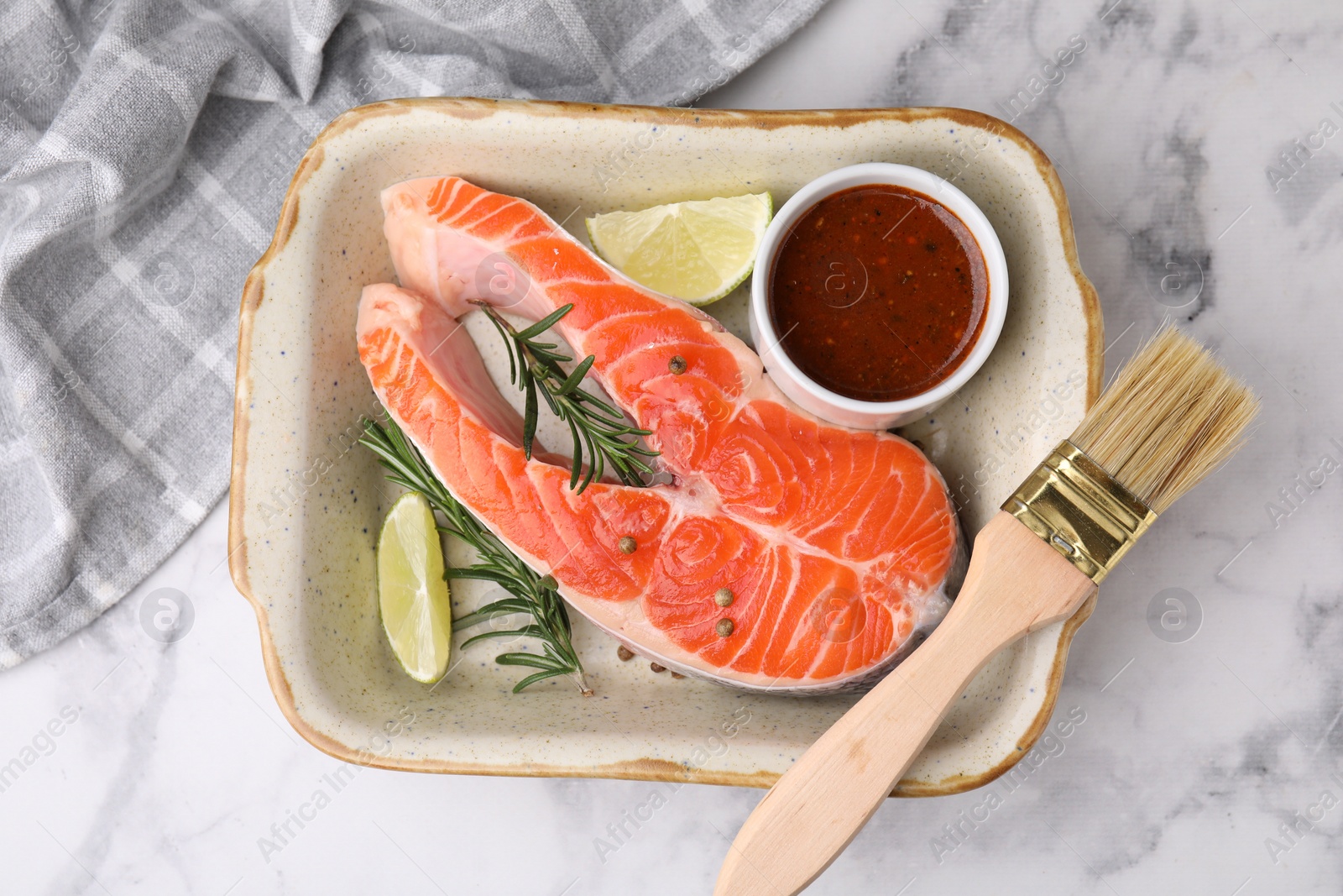 Photo of Fresh fish, lime, rosemary and marinade in baking dish on light marble table, top view