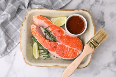 Photo of Fresh fish, lime, rosemary and marinade in baking dish on light marble table, top view