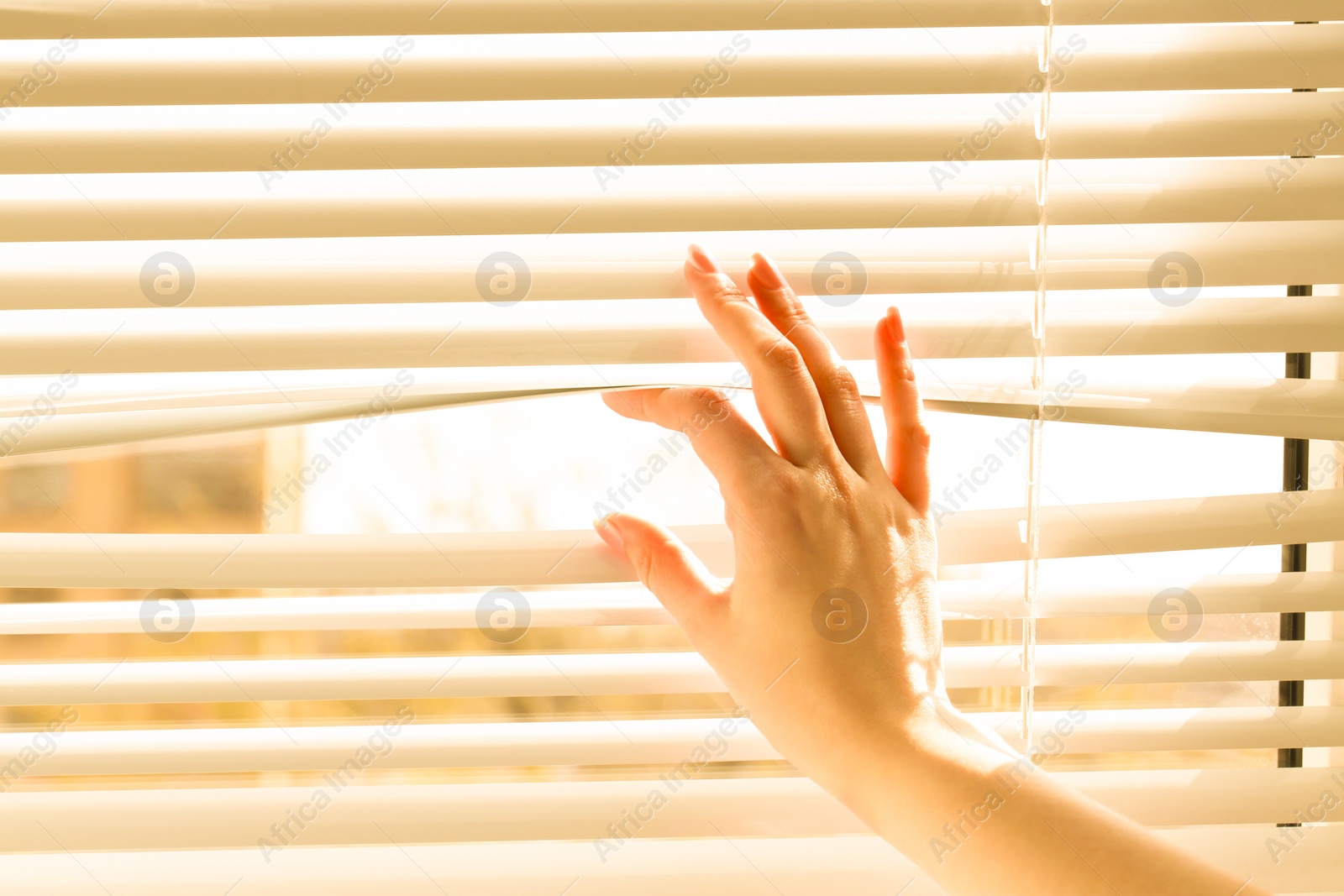 Photo of Woman separating slats of white blinds indoors, closeup