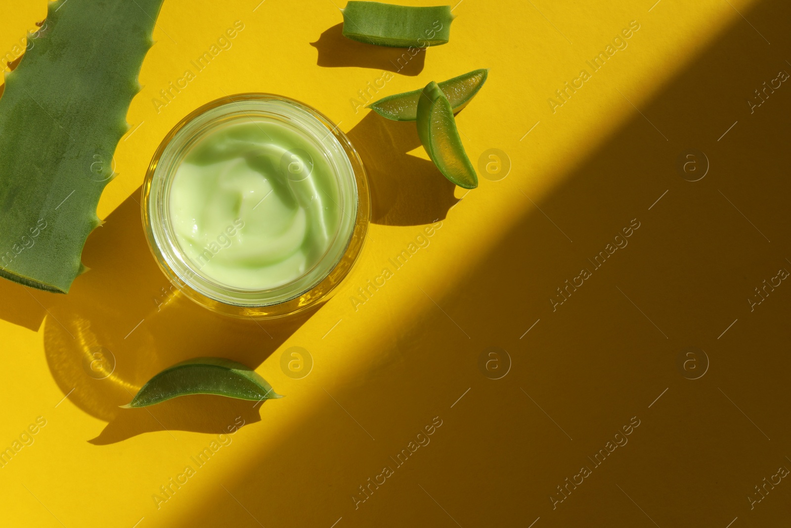 Photo of Jar with cream and cut aloe leaves on yellow background, flat lay. Space for text