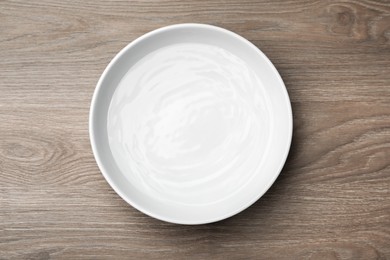 Photo of White bowl with water on wooden table, top view