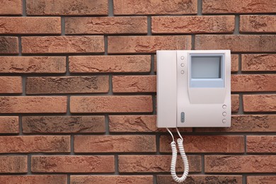 Photo of Modern intercom system with handset on red brick wall, space for text