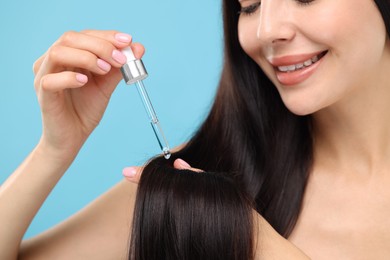 Beautiful woman applying hair serum on light blue background, closeup. Cosmetic product