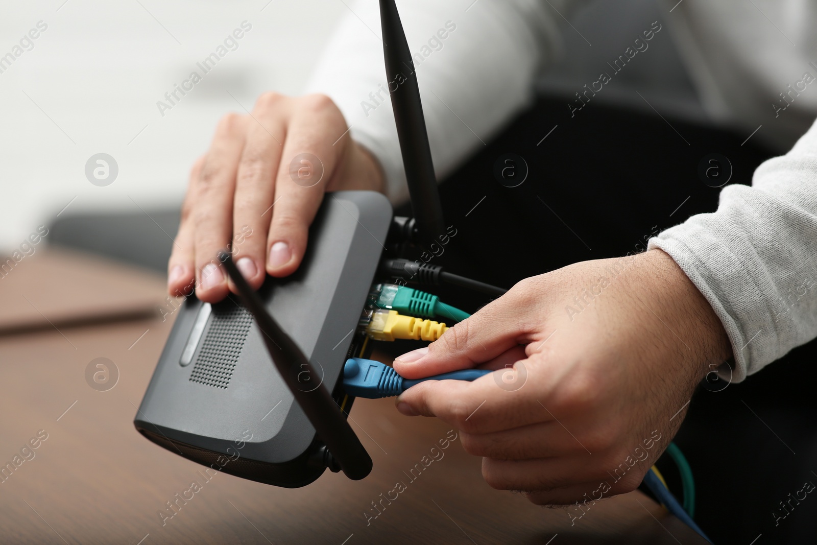 Photo of Man inserting cable into Wi-Fi router at wooden table indoors, closeup