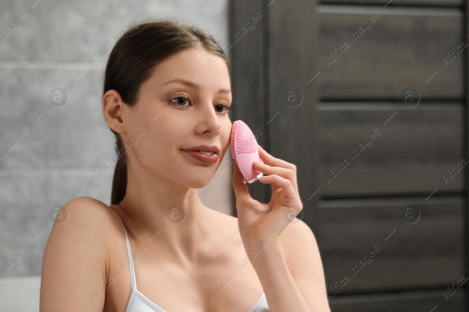Photo of Washing face. Young woman with cleansing brush in bathroom, space for text