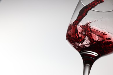 Pouring tasty red wine in glass on white background, closeup. Space for text