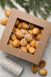 Photo of Delicious nut shaped cookies with boiled condensed milk in box and fir branch on white wooden table, flat lay