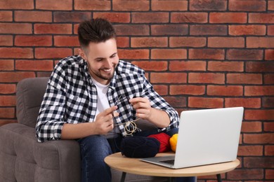 Photo of Happy man learning to knit with online course on laptop at home. Time for hobby