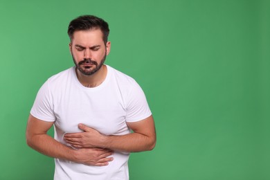 Photo of Unhappy man suffering from stomach pain on green background, space for text