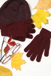 Flat lay composition with stylish woolen gloves and dry leaves on white wooden table