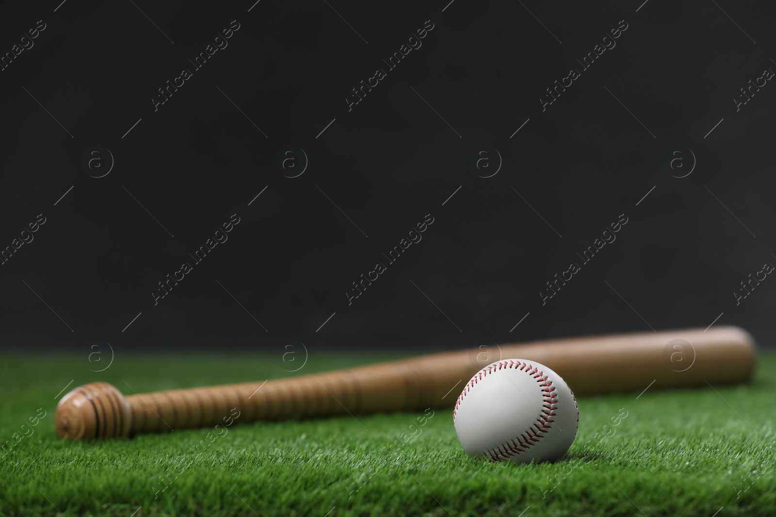 Photo of Baseball bat and ball on green grass against dark background. Space for text