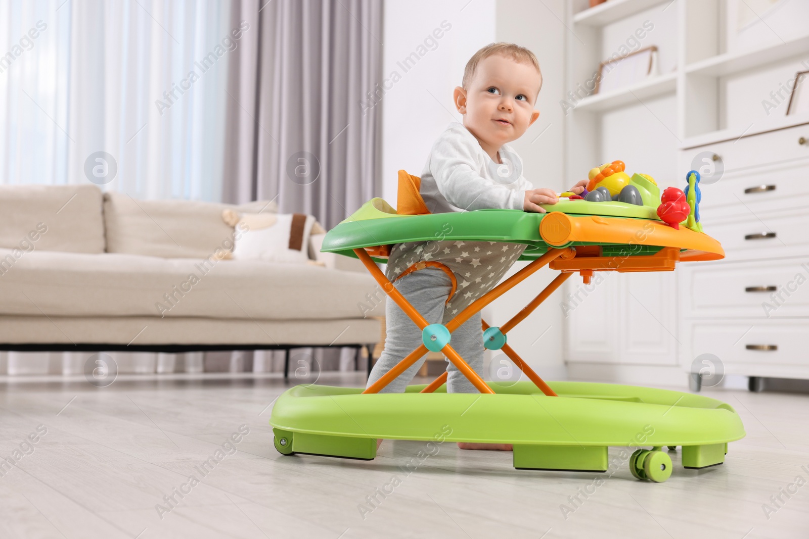 Photo of Cute little boy making first steps with baby walker at home