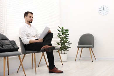 Man with sheet of paper waiting for job interview indoors