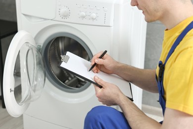 Photo of Plumber writing results of examining washing machine in bathroom, closeup