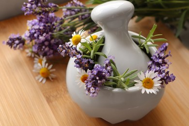 Mortar with fresh lavender, chamomile flowers, rosemary and pestle on wooden table