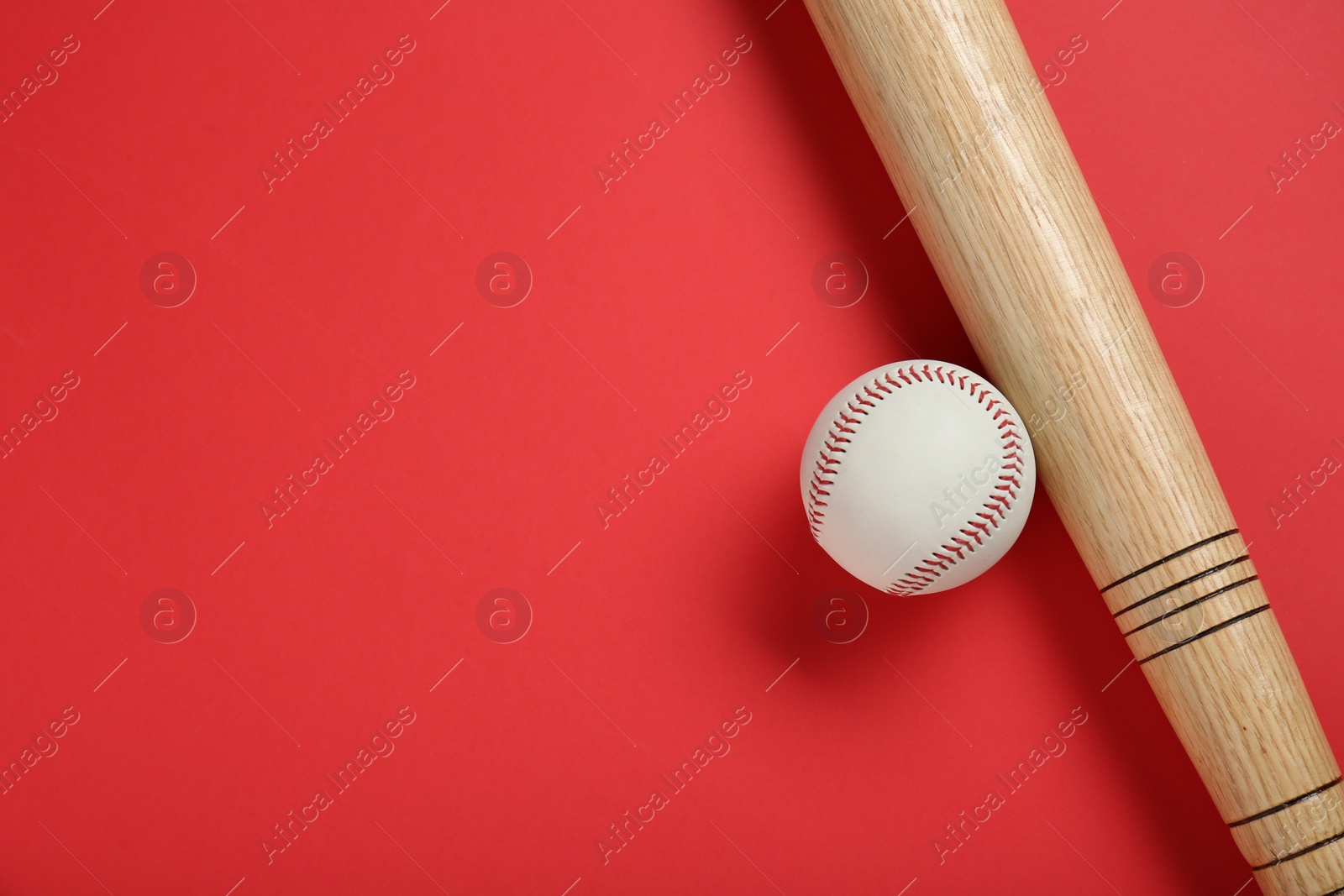 Photo of Wooden baseball bat and ball on red background, flat lay. Space for text