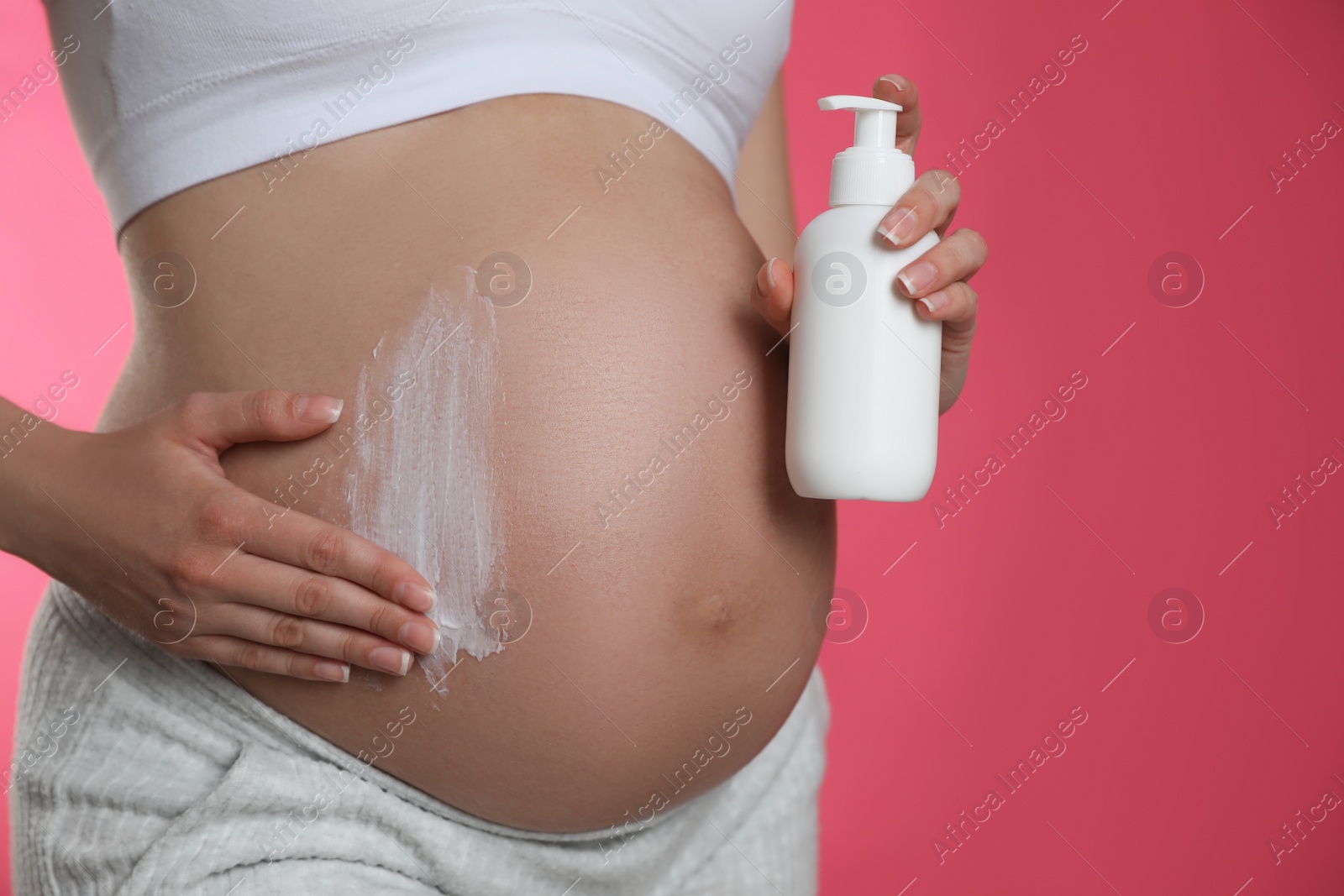 Photo of Young pregnant woman with cosmetic product on pink background, closeup. Space for text