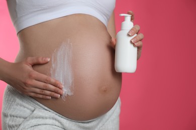 Young pregnant woman with cosmetic product on pink background, closeup. Space for text