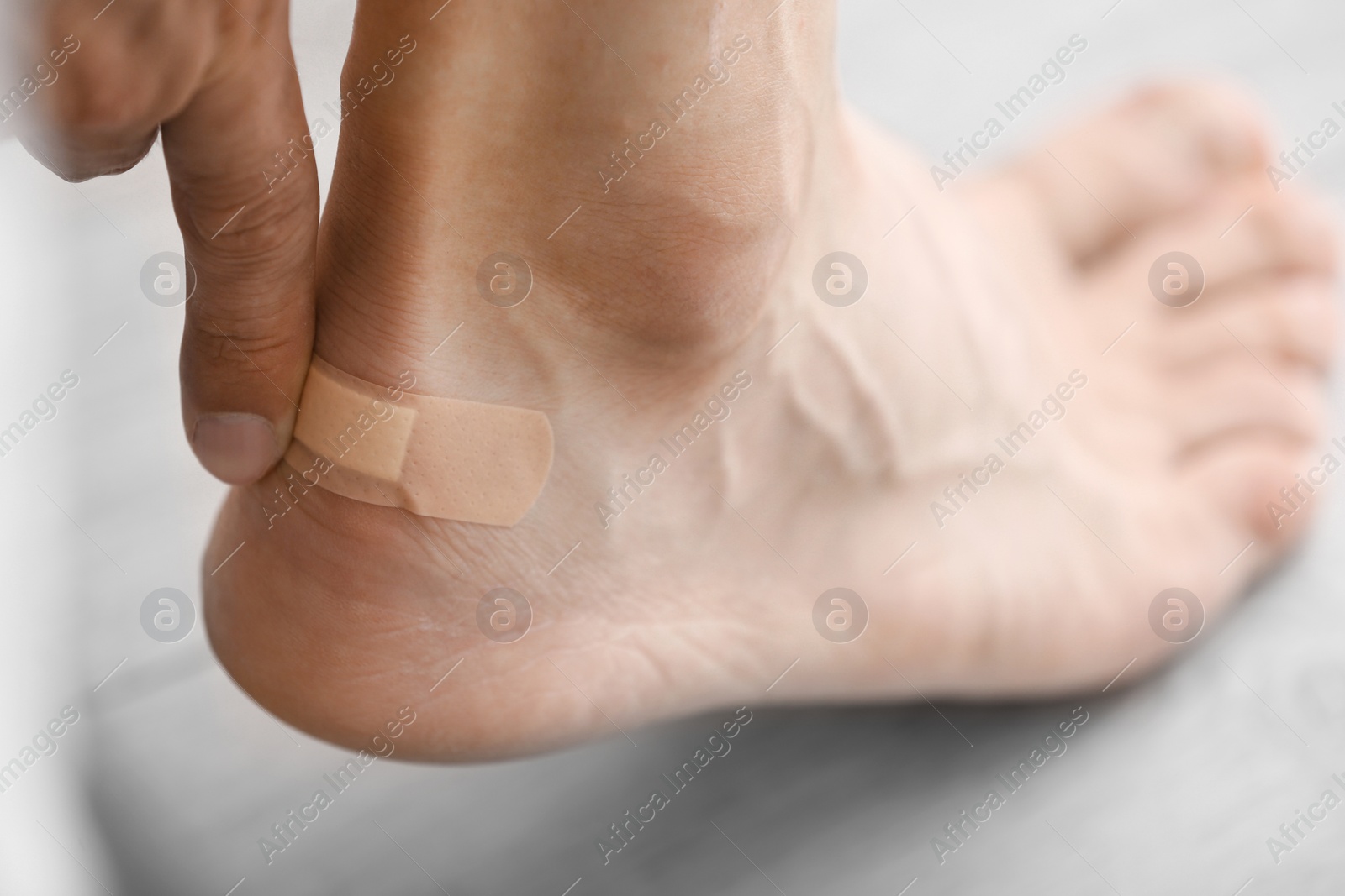 Photo of Man applying adhesive bandage on heel indoors, closeup