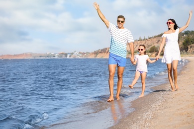 Photo of Happy family walking on sandy beach near sea. Summer holidays