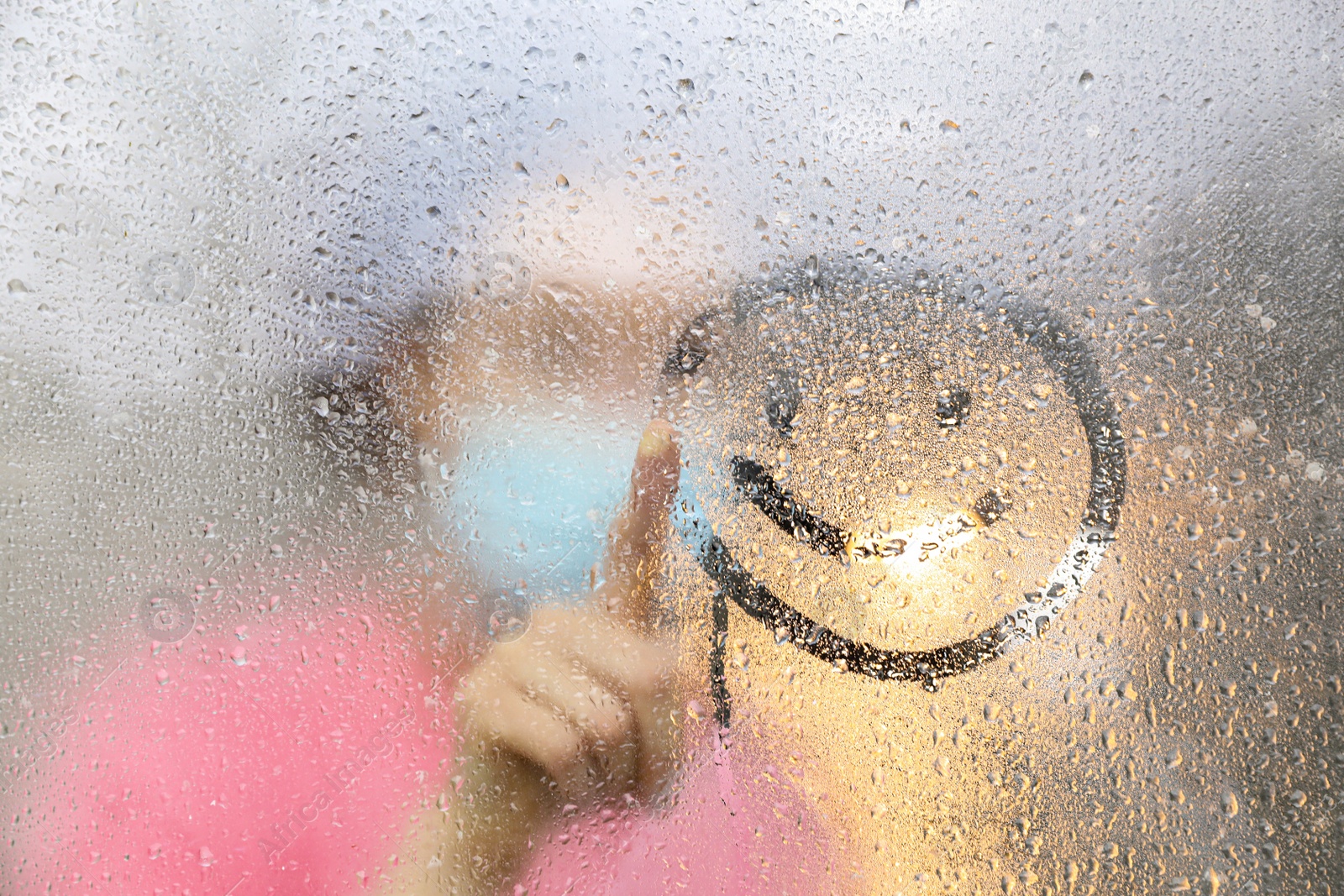 Photo of Woman drawing happy face on foggy window at rainy weather, closeup