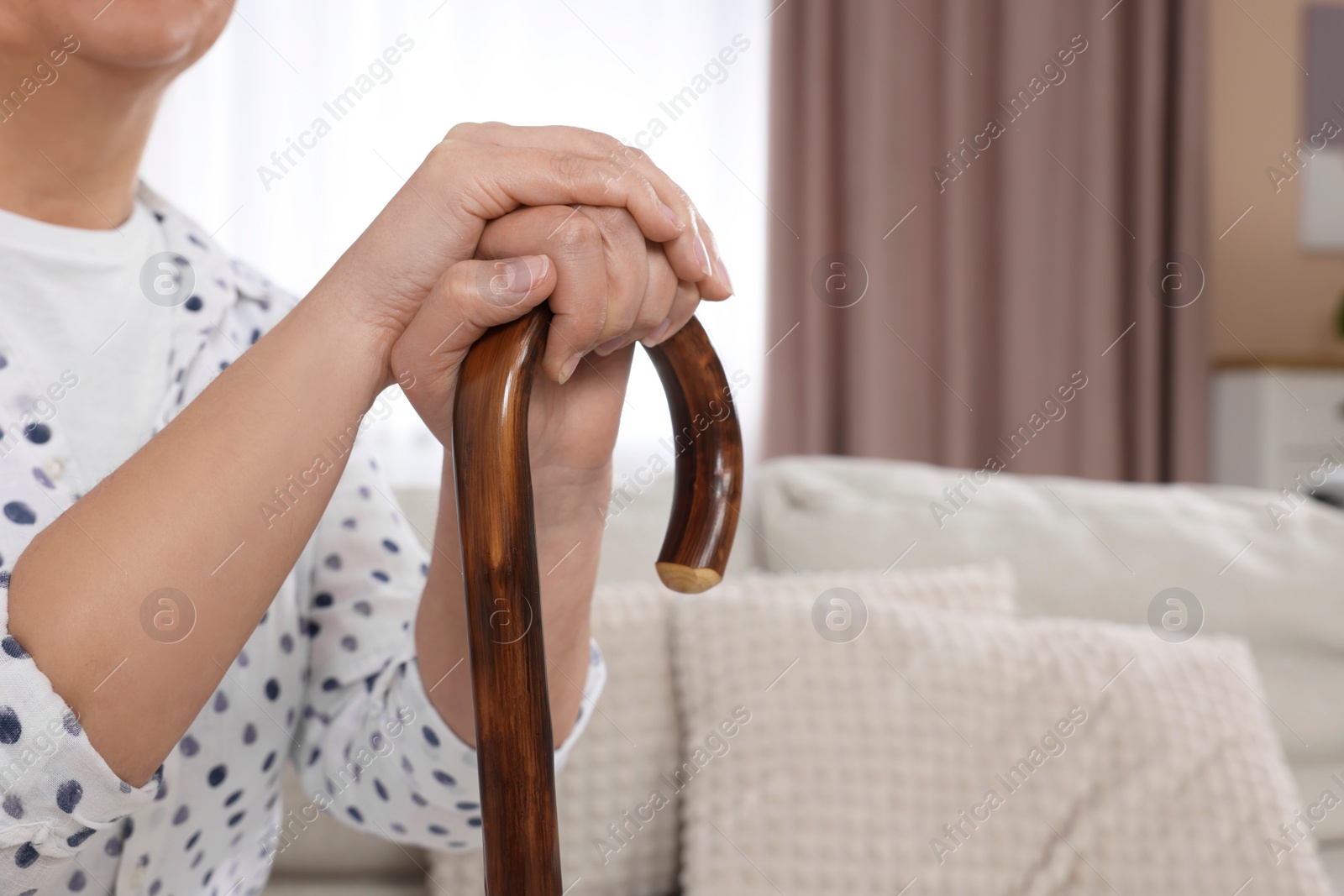 Photo of Senior woman with walking cane sitting on sofa at home, closeup. Space for text