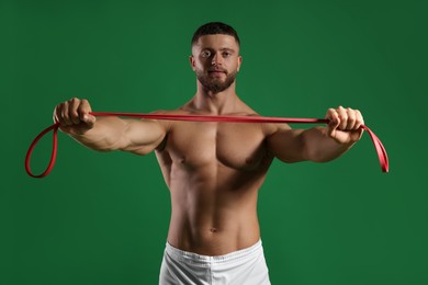 Photo of Muscular man exercising with elastic resistance band on green background