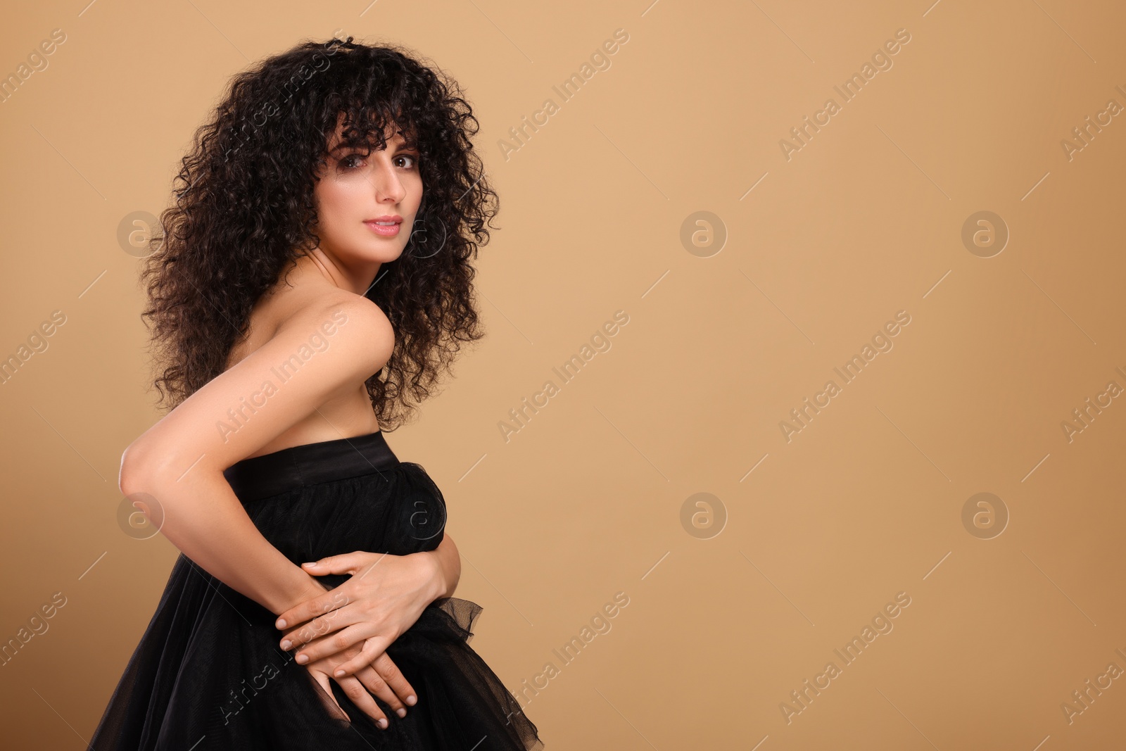 Photo of Beautiful young woman with long curly hair on beige background. Space for text