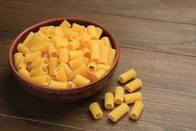 Raw rigatoni pasta in bowl on wooden table, closeup. Space for text